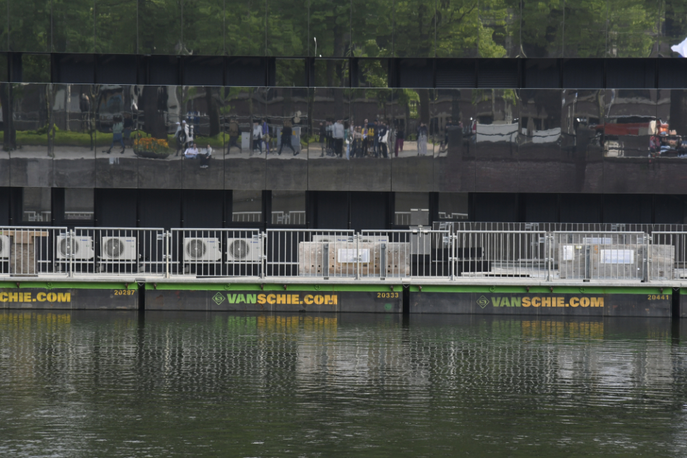 group mirrored in temporary building facade across the water